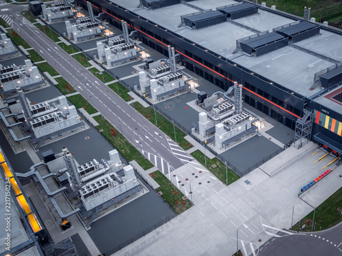 Aerial view of a modern data center facility featuring multiple HVAC cooling units on flat rooftops, paved service roads, and a large warehouse building in The Netherlands.