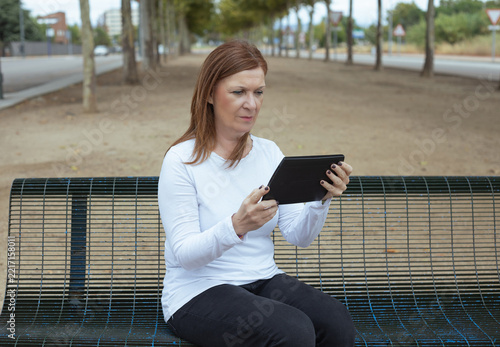 Mature woman using digital tablet sitting on a park bench