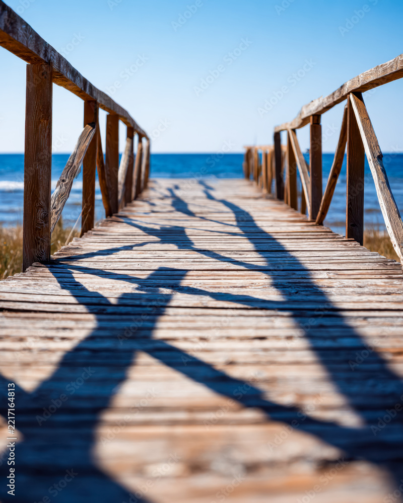 Fototapeta premium Wooden pier leading to the ocean with shadow patterns on the planks