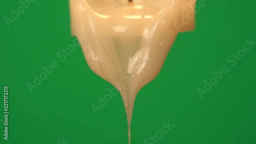 Molten white wax dripping slowly from a burning candle wick against a vibrant green surface creates an evocative scene representing passing time rituals tranquility meditation warmth and
