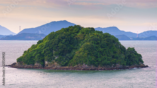 Yatsushiro, Kumamoto Pref, Japan - Oct 9 2024, panoramic aerial view of an uninhabited island covered with forest off coast of Yatsushiro, at daytime with cloudy sky, Yatsushiro, Japan