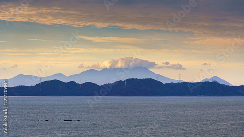 Yatsushiro, Kumamoto Pref, Japan - Oct 9 2024, panoramic view of sea in foreground, and in background a coastline of forested mountains, with power towers installed along coast, Yatsushiro, Japan