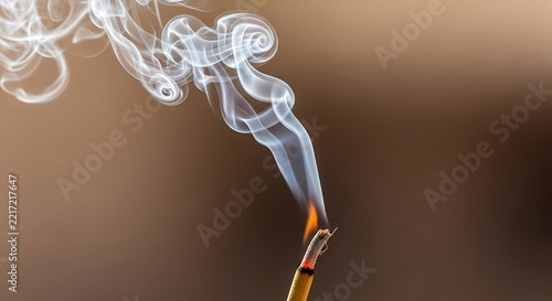 Thin trail of white smoke rising from a burning incense stick on a brown background