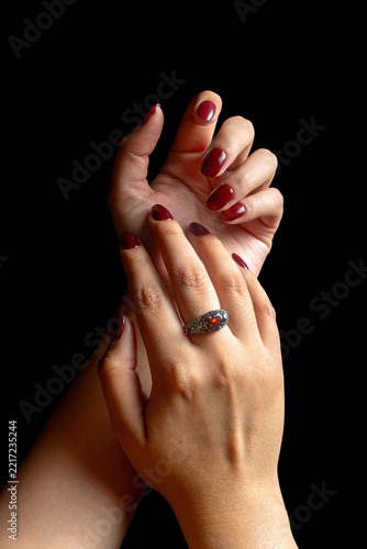 Elegant Female Hands with Burgundy Nail Polish and Vintage Ring on Black Background