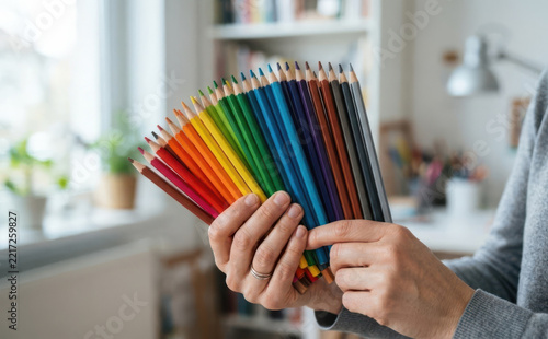 Woman holding rainbow colored pencils in a bright room representing creativity and art supplies