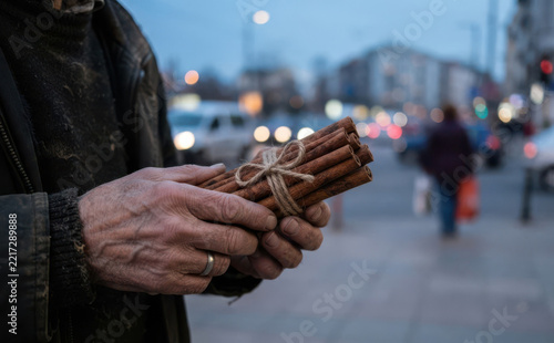 Elderly man holding a bundled bundle of cinnamon sticks on a city street representing poverty