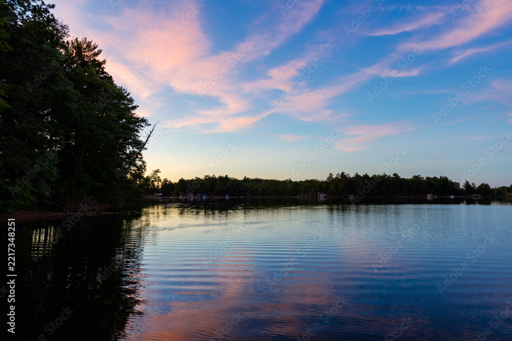 Fototapeta premium Serene Lake Sunset Landscape with Pink Cirrus Clouds Reflected on Calm Water and Forest Shoreline Silhouette