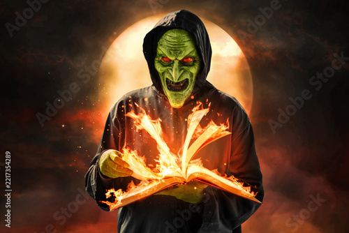 Scary witch holding burning magic spellbook at night with full moon, Halloween theme