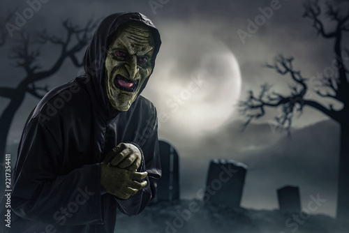 Portrait of scary witch on graveyard at night with full moon, Halloween theme