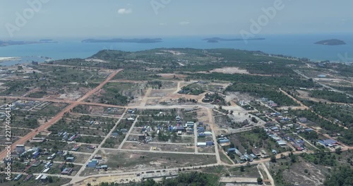 Forward aerial reveals the scale of a coastal land development project, where an intricate network of dirt roads fragments the terrain, while in the distance, the sea mist and islands blend into the h