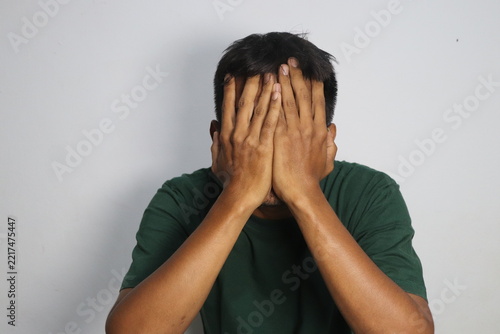 Stressed young man hiding face in hands expressing grief and despair