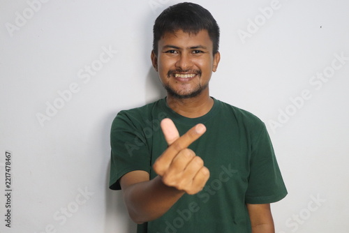 Young man smiling and making mini heart hand sign against white wall