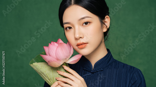 Beautiful young Asian woman holding a pink lotus flower against a green background