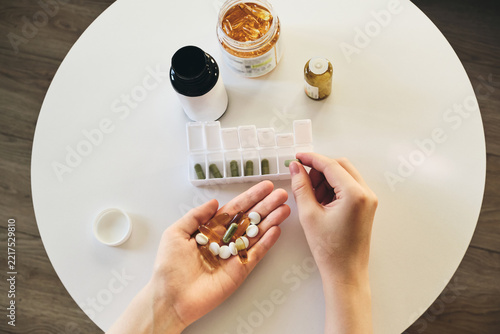 Hands arranging different medications and vitamins into weekly pill dispenser for health management