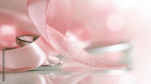 National Mammography Day: macro photograph of a satin pink awareness ribbon draped over a silver stethoscope on a clean white surface, delicate fabric folds, tiny water droplets
