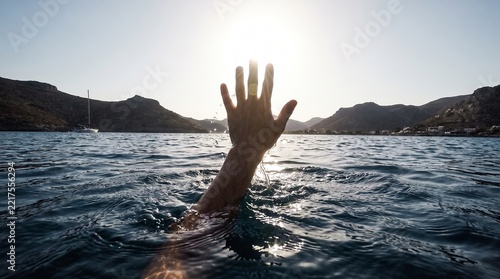 Drowning person hand reaching out for help in the sea water against sunlight
