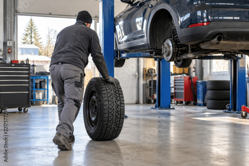Mechanic rolling a winter tire toward a car on a lift - seasonal tire changeover service in auto repair shop