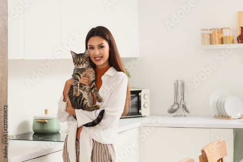 Pet ownership and companionship, happy young woman holding a tabby cat in a m...