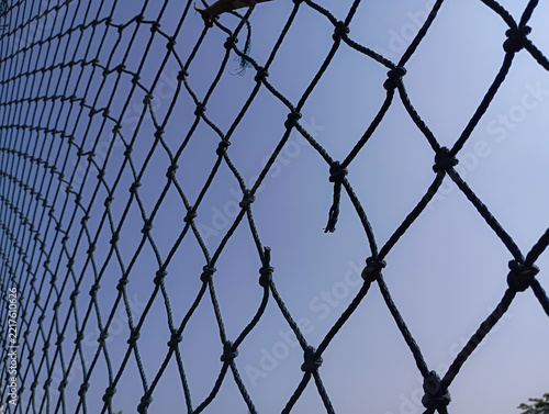 Broken black rope net against clear blue sky