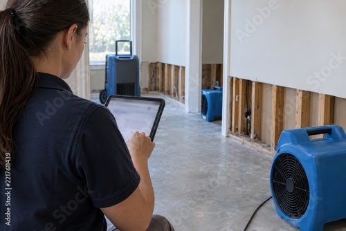 woman monitors drying equipment inside a damaged home