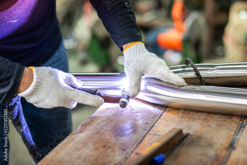 Selective focus to a worker performing precise TIG welding on stainless steel pipe parts in a factory workshop. Craftsmanship in metal fabrication and pipe welding process.