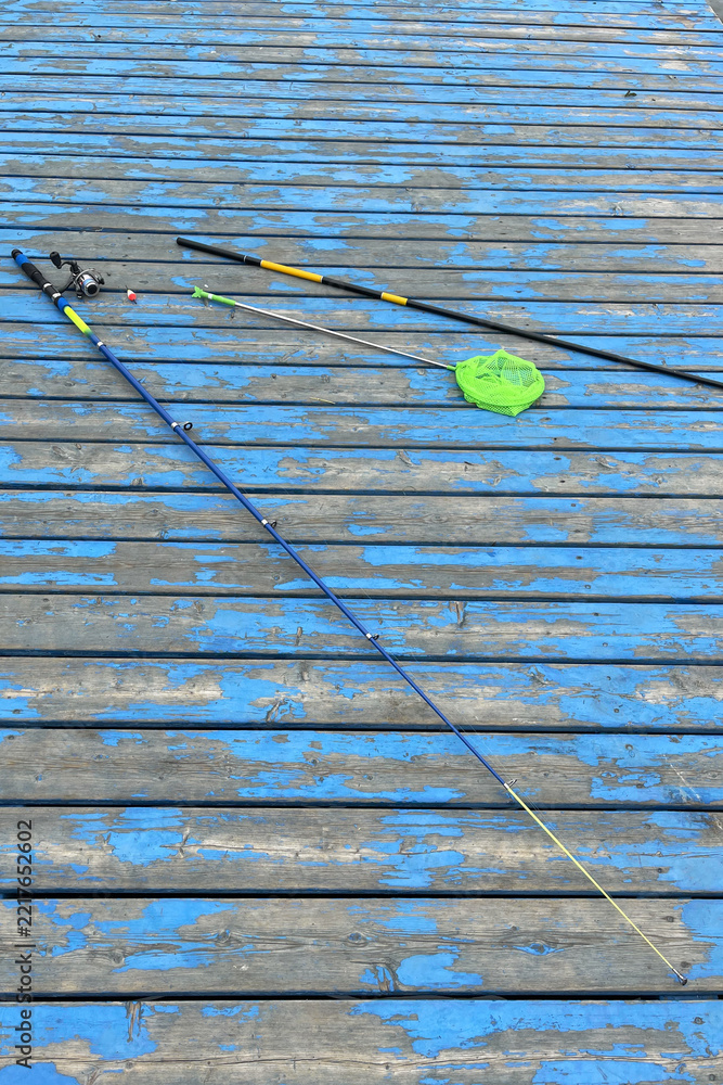 Fototapeta premium Fishing gear rests on a blue wooden dock beside the water in a sunny setting during the afternoon hours