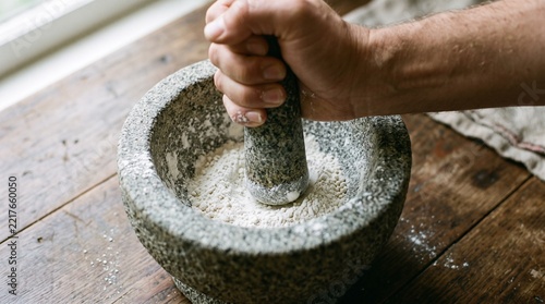 Rustic stone mortar and pestle grinding white powder, hand crushing ingredients on wooden table, traditional kitchen tool for spices