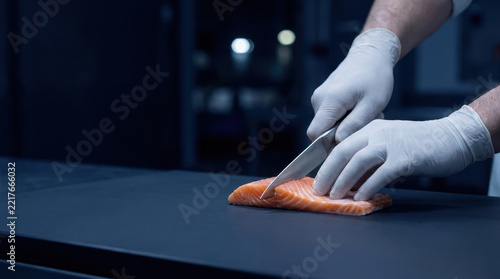 Salmon food security solutions support hygienic preparation by gloved chef using sharp knife on dark kitchen counter