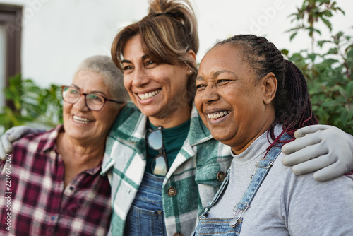 Happy multiracial senior women hugging each other outdoor during fall season - Elderly people, friendship and diversity concept - Focus on african woman face