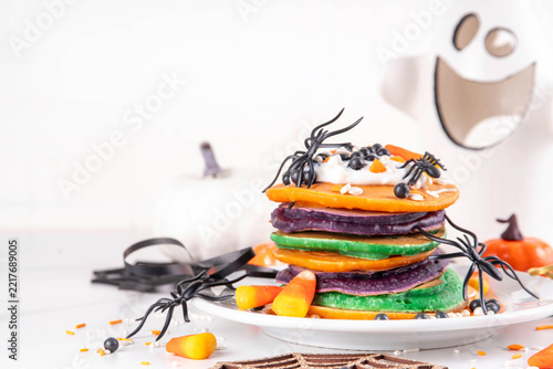 Colorful Halloween Pancakes with candy, pumpkin spider decoration. Stack of bright colored pancakes, with whipped cream, ready for Halloween breakfast or brunch