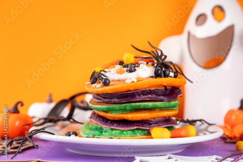 Colorful Halloween Pancakes with candy, pumpkin spider decoration. Stack of bright colored pancakes, with whipped cream, ready for Halloween breakfast or brunch