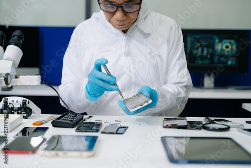 Professional technician in blue gloves repairing a dismantled smartphone with a screwdriver in a high-tech lab. Precision electronics maintenance