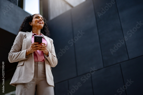 Thoughtful professional woman holding a smartphone and looking away outdoors, illustrating decision making, planning, business strategy and focused communication