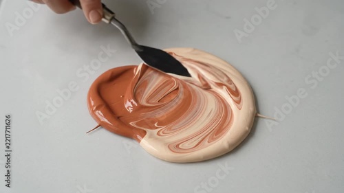 Hand with metal palette knife swirl together terracotta and cream acrylic paints on a clean surface, Close Up, 4K