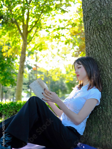 Beautiful Young Woman Reading Book While Leaning Against Tree Trunk in Park, Relaxing Girl Enjoying Literature in Green Nature Footage, Lifestyle Outdoor Leisure Concept Video, Peaceful Reading Scene