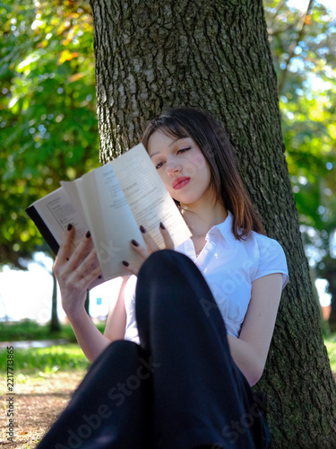 Beautiful Young Woman Reading Book While Leaning Against Tree Trunk in Park, Relaxing Girl Enjoying Literature in Green Nature Footage, Lifestyle Outdoor Leisure Concept Video, Peaceful Reading Scene