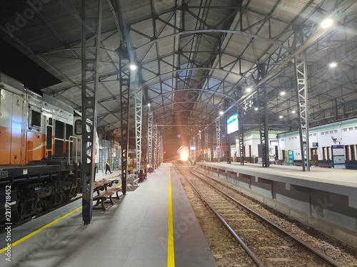 Modern Railway Station Platform at Night with Train Locomotive and Overhead Steel Truss Architecture
