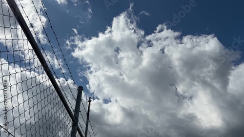青空と流れる白い雲、有刺鉄線のアクセントが映える明るいタイムラプス風景