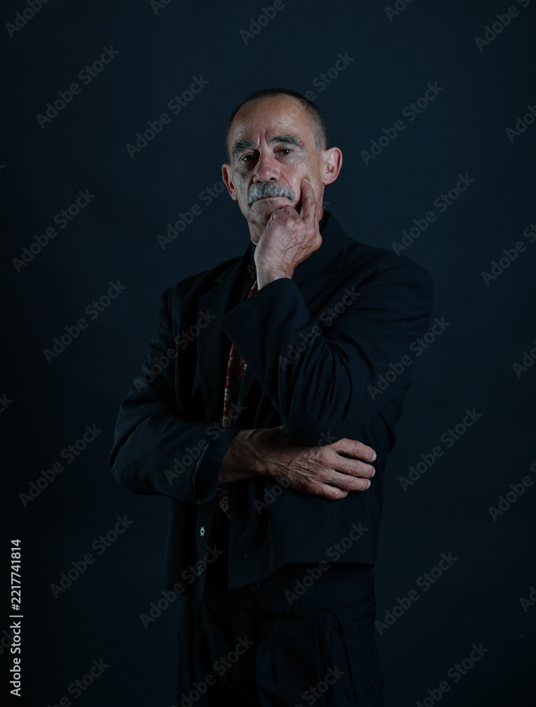 Naklejka premium Nachdenkliches Charakterporträt eines älteren Mannes in dunkler Kleidung mit fester, selbstbewusster Pose. Stärke, Persönlichkeit, Lebenserfahrung, Entschlossenheit und dramatische Studiofotografie.