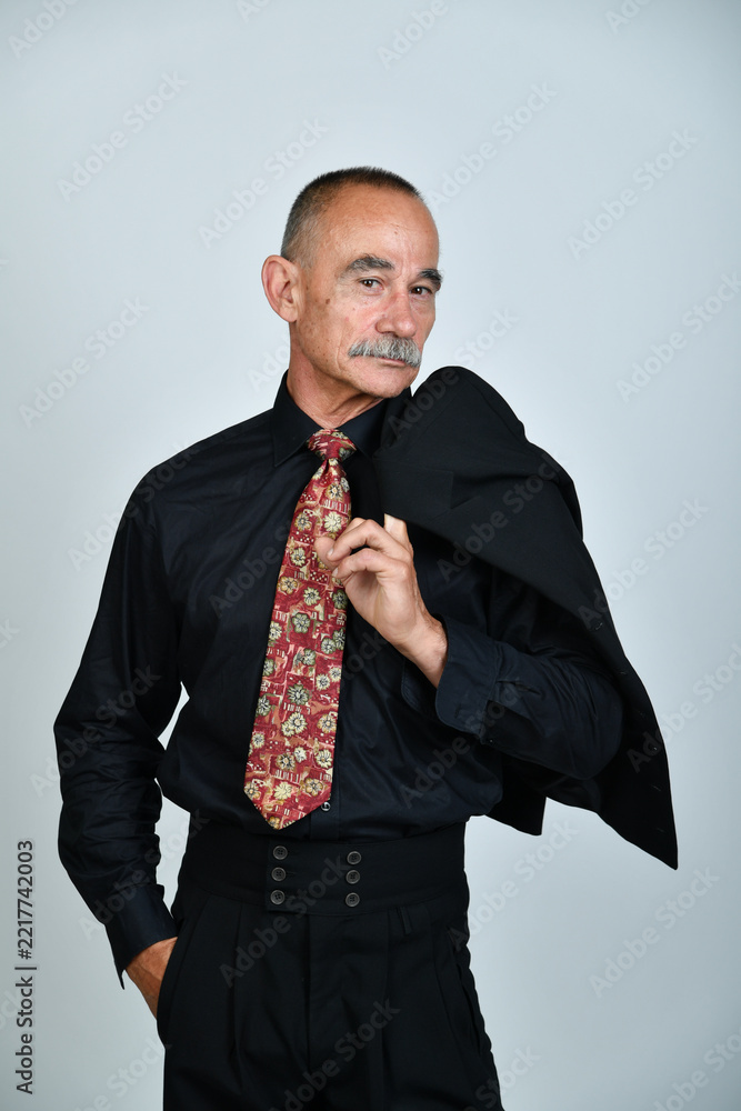 Naklejka premium Charakterporträt eines älteren Mannes im schwarzen Hemd mit gemusterter Krawatte und Sakko über der Schulter. Selbstbewusst, elegant, Business, Persönlichkeit und moderne Studiofotografie.
