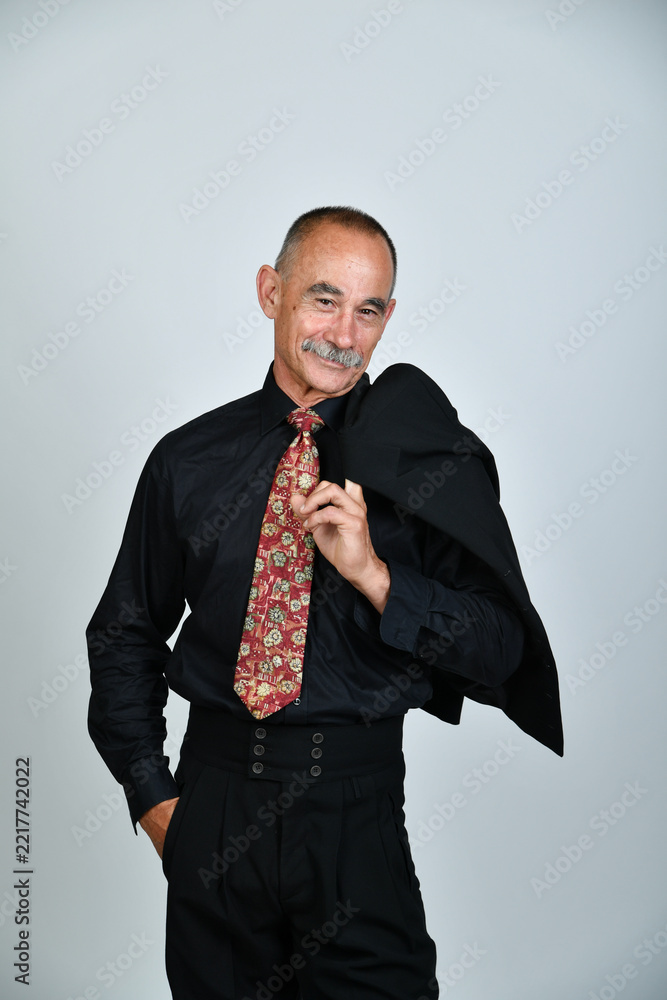 Naklejka premium Charakterporträt eines älteren Mannes im schwarzen Hemd mit gemusterter Krawatte und Sakko über der Schulter. Selbstbewusst, elegant, Business, Persönlichkeit und moderne Studiofotografie.
