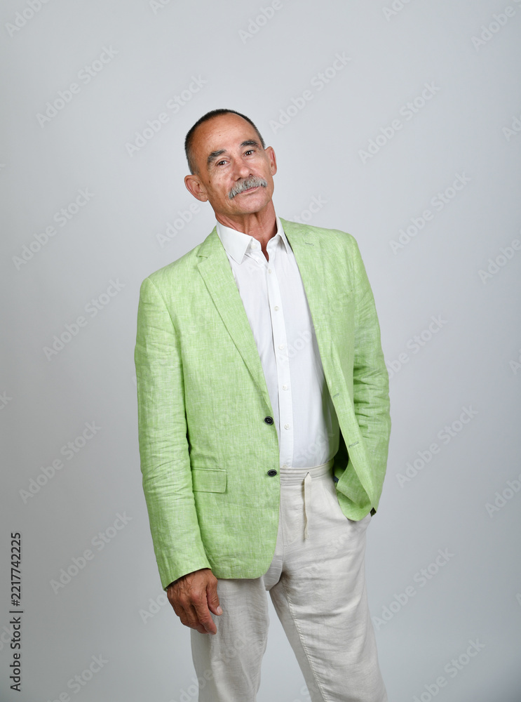 Naklejka premium Charakterporträt eines älteren Mannes im hellgrünen Sakko und weißer Kleidung vor neutralem Hintergrund. Best Ager, sommerliche Eleganz, Persönlichkeit, Fashion und moderne Studiofotografie.