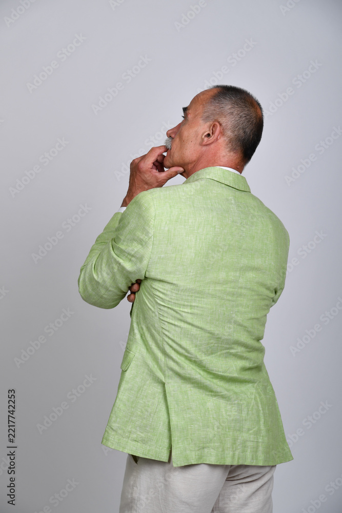 Naklejka premium Rückansicht eines älteren Mannes im hellgrünen Sakko mit nachdenklicher Hand am Kinn. Best Ager, Charakterporträt, Sommermode, Gentleman-Stil, Persönlichkeit und moderne Studiofotografie.