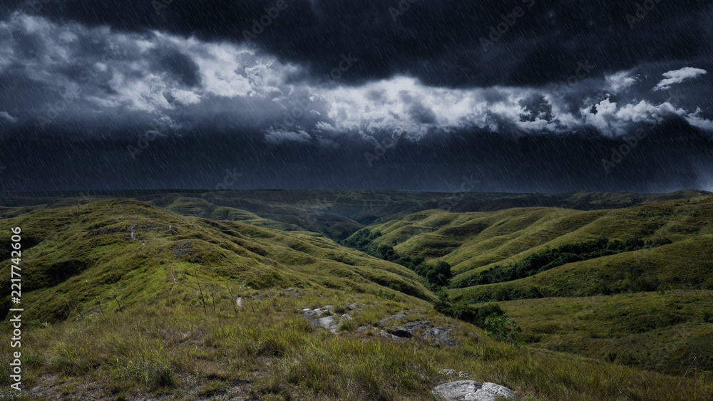 Naklejka premium Dramatic stormy sky with heavy rain falling over rolling green hills and valleys in a rural landscape, creating a moody and atmospheric natural scene. Storm or bad weather background