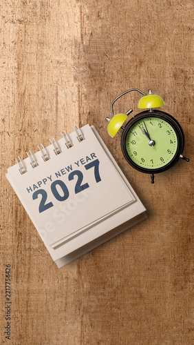 Happy New Year 2027 calendar and green alarm clock on textured wooden surface. Happy New Year 2027