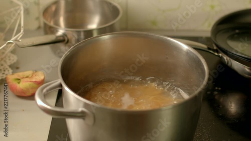 Stainless steel pot filled with boiling water and pasta simmers on stovetop in home kitchen, steam rising and warm light reflecting off metal surface.