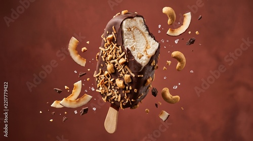 Chocolate Covered Ice Cream Bar With Coconut And Cashew Nuts Floating On Dark Brown Background