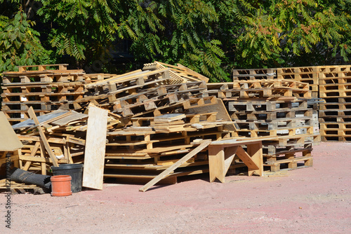 Large piles of old wooden industrial pallets and scrap wood stacked outdoors in an open storage area on a sunny day.