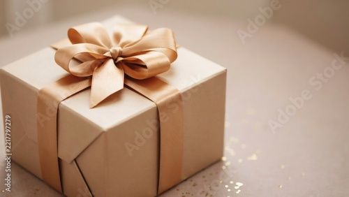 Elegant gift box wrapped in beige paper with a shiny golden ribbon bow on a festive background