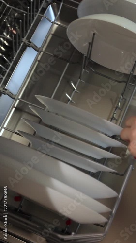 Vertical video. Woman takes a washed plate from dishwasher machine. Household domestic life. Close-up, top view.